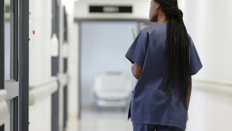Back-of-african-american-female-doctor-walking-in-hospital-corridor,-slow-motion
