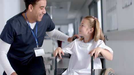 Biracial-doctor-talking-to-caucasian-girl-patient-sitting-in-wheelchair-in-hospital,-slow-motion