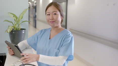 Retrato-De-Una-Feliz-Doctora-Asiática-Usando-Una-Tableta-En-La-Recepción-Del-Hospital,-Espacio-Para-Copiar,-Cámara-Lenta
