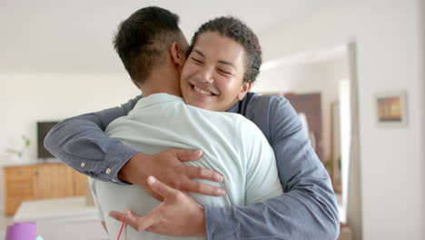 Happy-diverse-gay-male-couple-with-keys-to-new-house-embracing-in-living-room,-slow-motion