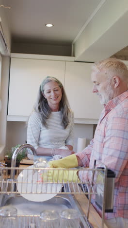 Vertical-video-of-happy-senior-caucasian-couple-washing-dishes-in-kitchen,-slow-motion