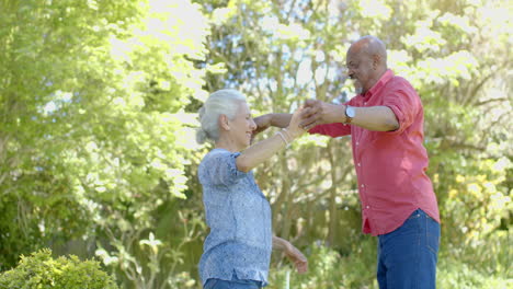 Happy-senior-biracial-couple-dancing-in-sunny-garden-at-home,-slow-motion