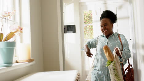 Happy-african-american-senior-woman-entering-house-with-shopping-in-sunny-room,-slow-motion