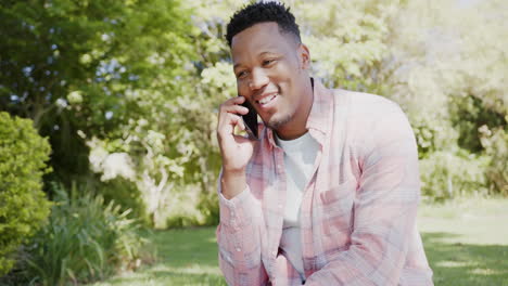 Feliz-Hombre-Afroamericano-Hablando-Por-Teléfono-Inteligente-En-El-Jardín-De-Casa,-Cámara-Lenta