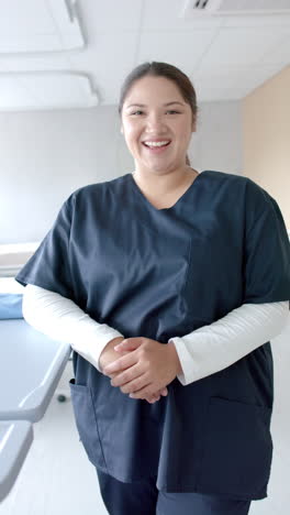 Vertical-video-portrait-of-plus-size-caucasian-female-doctor-smiling-in-hospital-ward,-slow-motion