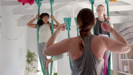 Diverse-fitness-teenage-girls-in-aerial-yoga-class-with-female-coach-in-big-white-room,-slow-motion