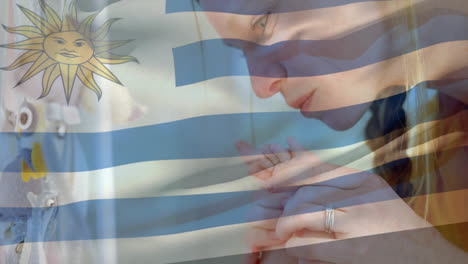 Animation-Der-Uruguayischen-Flagge-über-Einer-Kaukasischen-Mutter,-Die-Die-Füße-Ihres-Babys-Küsst