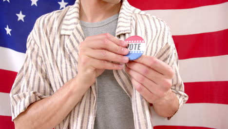 Midsection-of-biracial-man-in-front-of-american-flag-pinning-on-badge-with-vote-text,-slow-motion