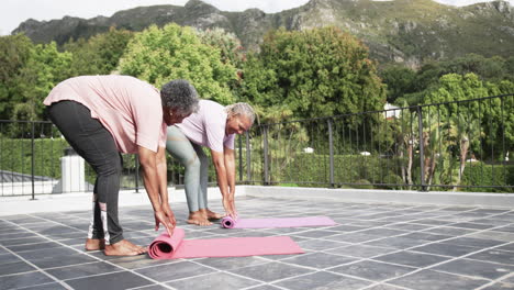 Senior-african-american-female-friends-unrolling-yoga-mats-on-balcony,-copy-space,-slow-motion