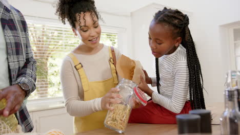 Happy-african-american-parents-and-daughter-pouring-pasta-into-jar-at-home,-slow-motion