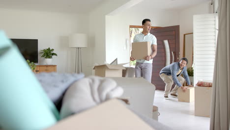 Happy-diverse-gay-male-couple-carrying-packing-boxes-into-new-home,-copy-space,-slow-motion