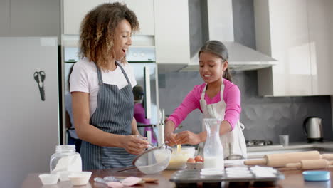 Happy-biracial-mother-and-daughter-making-cake-mix,-baking-in-kitchen,-slow-motion