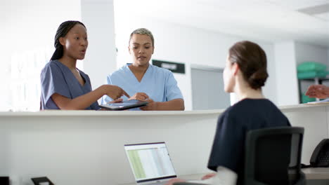 Diverse-female-doctors-discussing-work,-using-tablet-at-reception-desk-at-hospital,-slow-motion