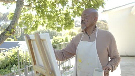 Happy-senior-biracial-man-painting-at-balcony-at-home,-slow-motion