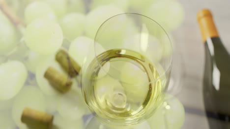 Composite-of-glass-of-white-wine-over-corks-and-white-grapes-on-white-background