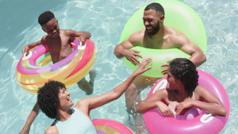 Happy-african-american-parents,-son-and-daughter-floating-on-inflatables-in-sunny-pool,-slow-motion