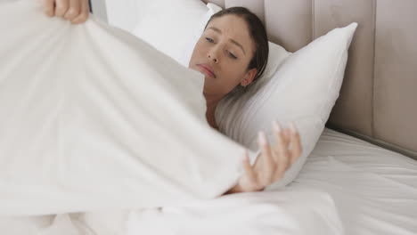 Sad-biracial-woman-lying-in-bed-holding-pillow-at-home,-slow-motion