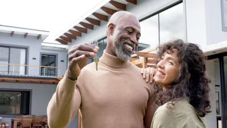 Portrait-of-happy-biracial-couple-embracing-and-holding-keys-at-new-house,-slow-motion