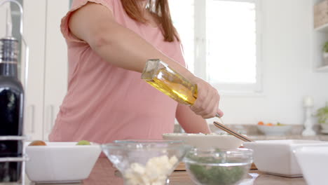 Happy-plus-size-biracial-woman-dressing-salad-with-olive-oil-in-kitchen,-copy-space,-slow-motion