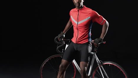 African-American-cyclist-poses-confidently-on-a-bicycle-on-a-black-background,-with-copy-space