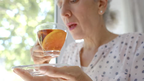Nachdenkliche-ältere-Frau-Mit-Gemischter-Abstammung,-Die-Zu-Hause-Am-Fenster-Tee-Trinkt,-Zeitlupe