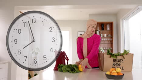 Biracial-woman-in-hijab-holding-vegetables-in-kitchen-over-clock