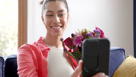 Fröhliches,-Gemischtrassiges-Teenager-Mädchen-Mit-Blumen,-Das-Zu-Hause-Einen-Smartphone-Videoanruf-Macht,-Zeitlupe
