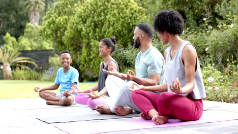 Happy-african-american-parents,-son-and-daughter-doing-yoga-meditation-in-garden,-slow-motion