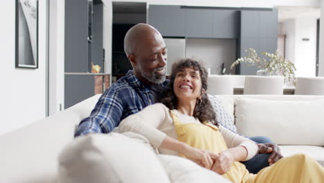 Portrait-of-happy-mature-diverse-couple-embracing-sitting-on-couch-in-living-room,-slow-motion