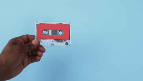 Video-of-african-american-man's-hand-holding-retro-tape-with-copy-space-on-blue-background