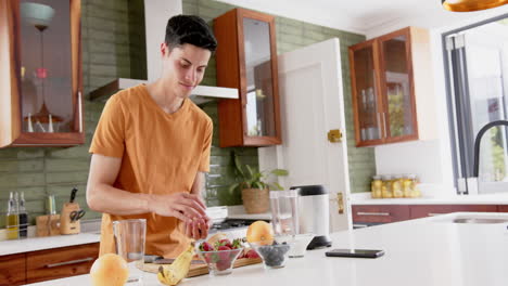 Happy-biracial-man-preparing-healthy-fruit-smoothie-with-blender-in-kitchen,-copy-space,-slow-motion