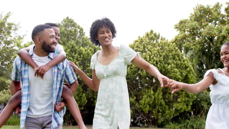 Happy-african-american-parents,-daughter-and-son-piggybacking-and-dancing-in-garden,-slow-motion