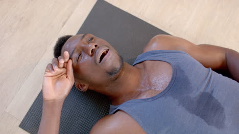 Tired-and-sweaty-african-american-man-lying-on-exercise-mat-in-sunny-living-room,-slow-motion