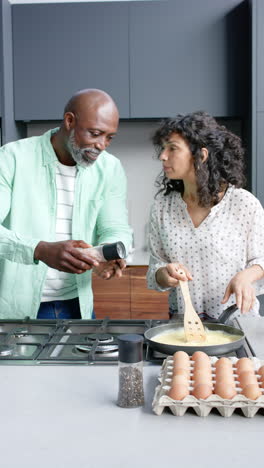 Vertikales-Video-Eines-Glücklichen-Biracial-Paares,-Das-In-Der-Küche-Das-Frühstück-Zubereitet,-Zeitlupe