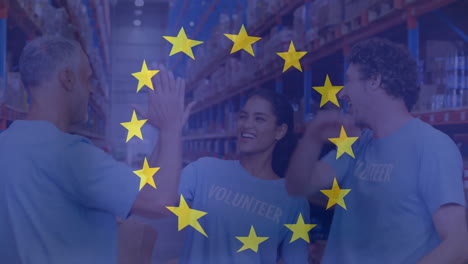 Animation-of-flag-of-european-union-over-diverse-male-and-female-volunteers-high-fiving-in-warehouse