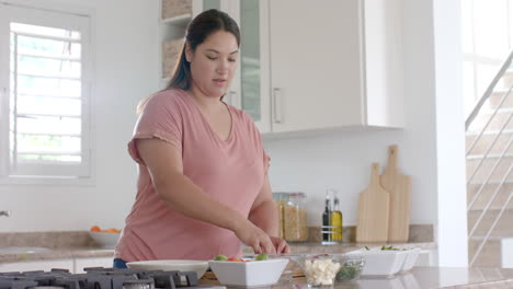 Happy-plus-size-biracial-woman-chopping-vegetables,-making-meal-in-kitchen,-copy-space,-slow-motion