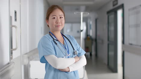 Portrait-of-happy-asian-female-doctor-wearing-scrubs-in-hospital-corridor,-slow-motion