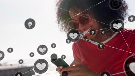 Animation-of-network-of-connections-with-icons-over-biracial-woman-using-smartphone
