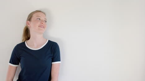 Happy-caucasian-woman-in-navy-blue-t-shirt-with-white-edging,-on-white-wall,-copy-space,-slow-motion