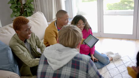 Happy-diverse-group-of-teenage-friends-using-tablet-and-talking-at-home,-slow-motion
