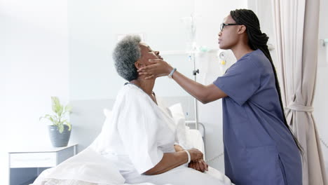 African-american-female-doctor-testing-eyes-of-senior-female-patient-in-hospital-room,-slow-motion