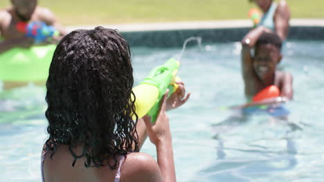 Happy-african-american-brother-and-sister-playing-with-water-pistols-in-sunny-pool,-slow-motion