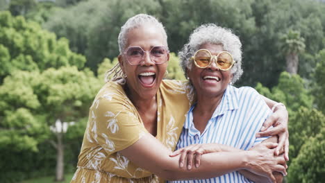 Portrait-of-senior-african-american-female-friends-in-sunglasses-hugging-in-garden,-slow-motion
