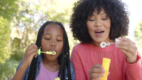 Glückliche-Afroamerikanische-Mutter-Mit-Tochter,-Die-Zu-Hause-Im-Garten-Seifenblasen-Bläst,-Zeitlupe