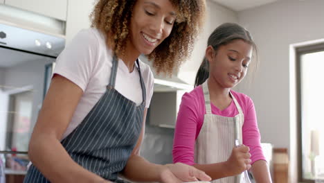 Happy-biracial-mother-and-daughter-kissing-while-baking-in-kitchen,-slow-motion