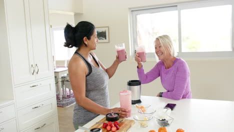 Two-happy-diverse-senior-women-toasting-with-cocktails-and-smiling-in-kitchen,-slow-motion