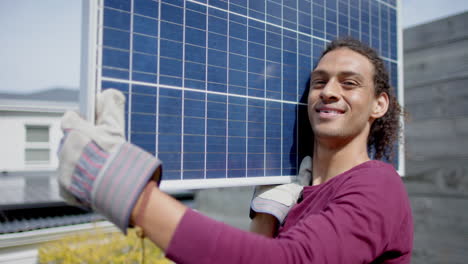 Portrait-of-happy-biracial-man-with-gloves-carrying-solar-panel-in-garden,-slow-motion