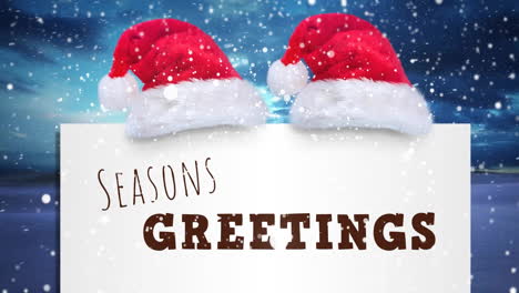 Animation-of-seasons-greetings-text-with-santa-claus-hats-and-snow-falling-over-winter-scenery