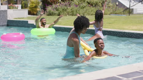 Happy-african-american-mother-teaching-son-to-swim-with-noodle-float-in-sunny-pool,-slow-motion