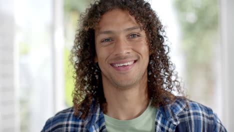 Portrait-of-happy-biracial-man-with-long-curly-dark-hair-smiling-at-home,-slow-motion